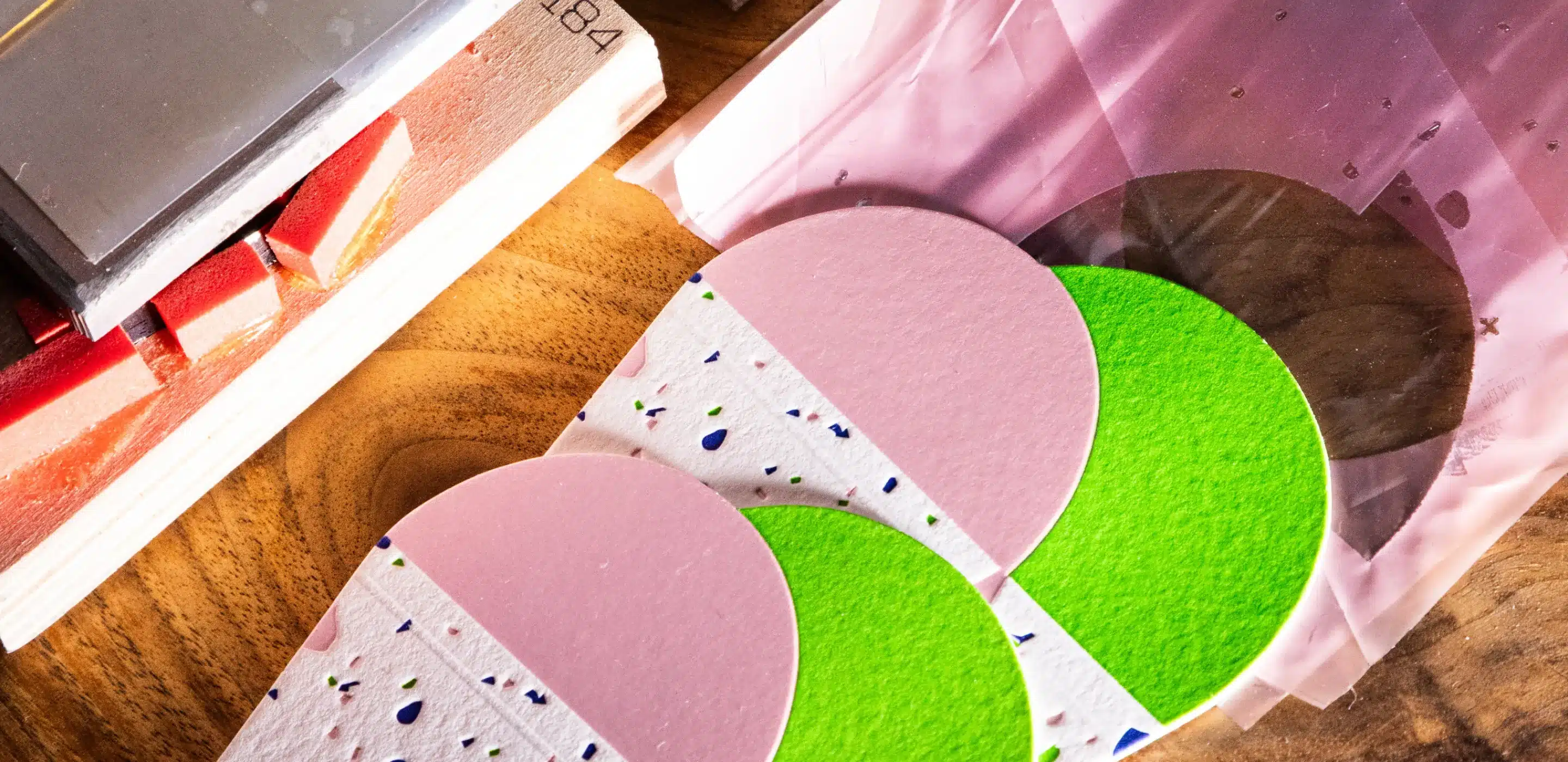 Colorful paper cutouts in pink and green on a wooden surface, with some transparent packaging and crafting materials…