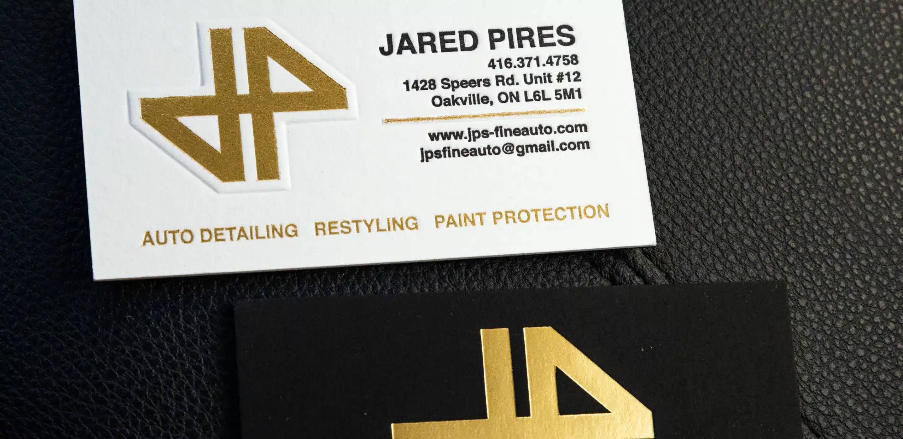 Two business cards, one white with gold text and logo, and one black with a gold logo, on a textured black surface.